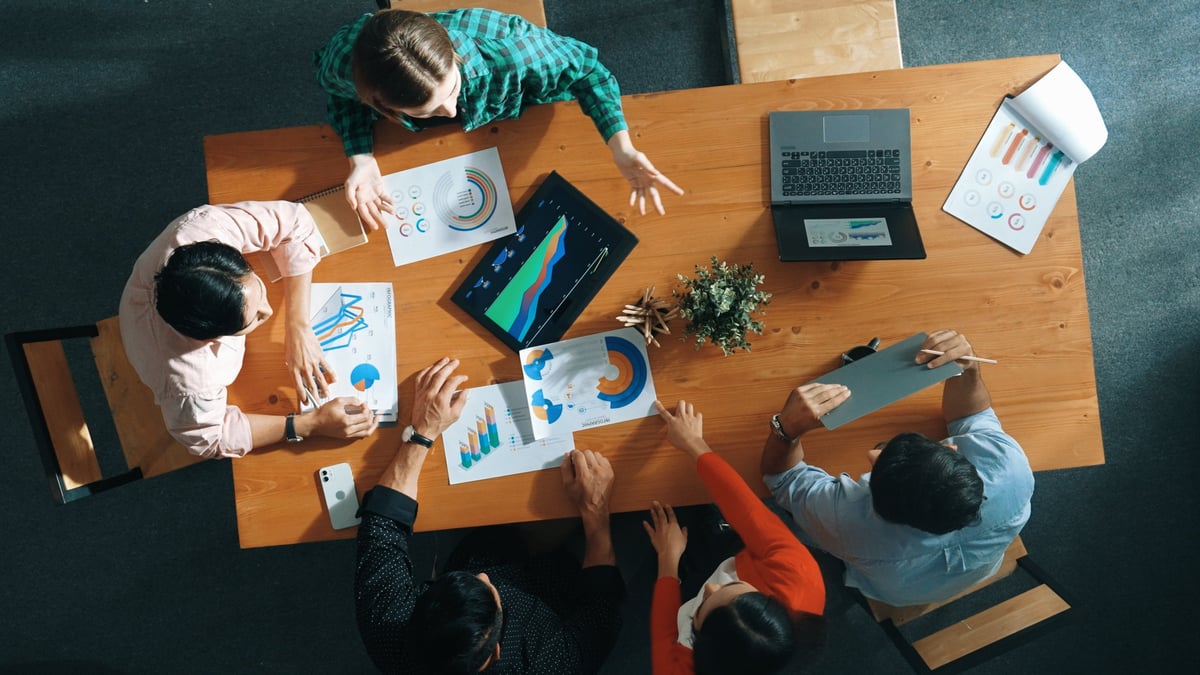 Ansicht von oben auf eine Geschäftsfrau, die Finanzdiagramme erklärt und präsentiert. Vielfältige Gruppe diskutiert und hört Präsentation über Aktienmarktstatistiken am Besprechungstisch mit Investitionsgraphen.