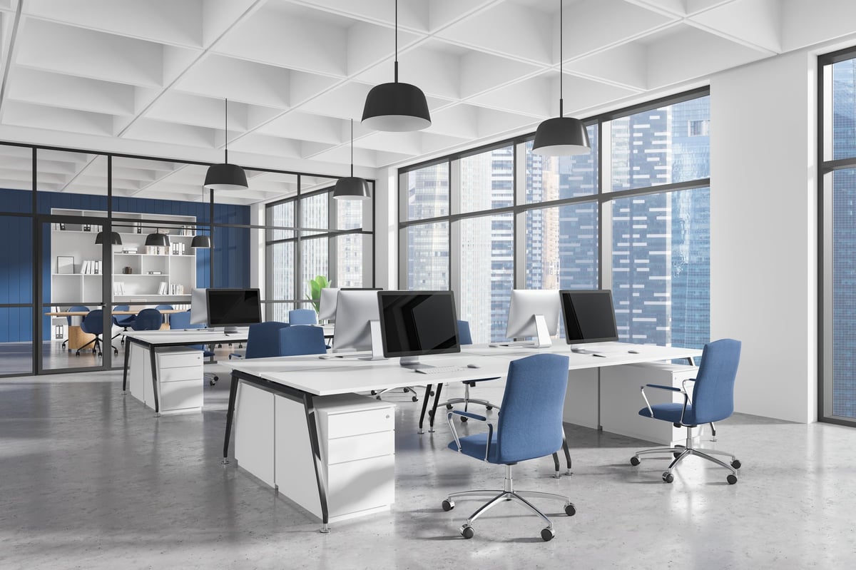 Zeitgemäßes Büroinnendesign mit ergonomischen Möbeln, blauen Stühlen, Schreibtischen und Computern in einem geräumigen Bereich mit großen Fenstern. Konzept der Arbeitsplatzgestaltung.